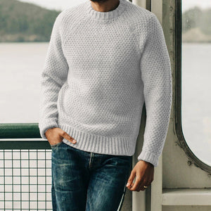 Man wearing light gray knitted men's pullover sweater with round neck and blue jeans indoors by window