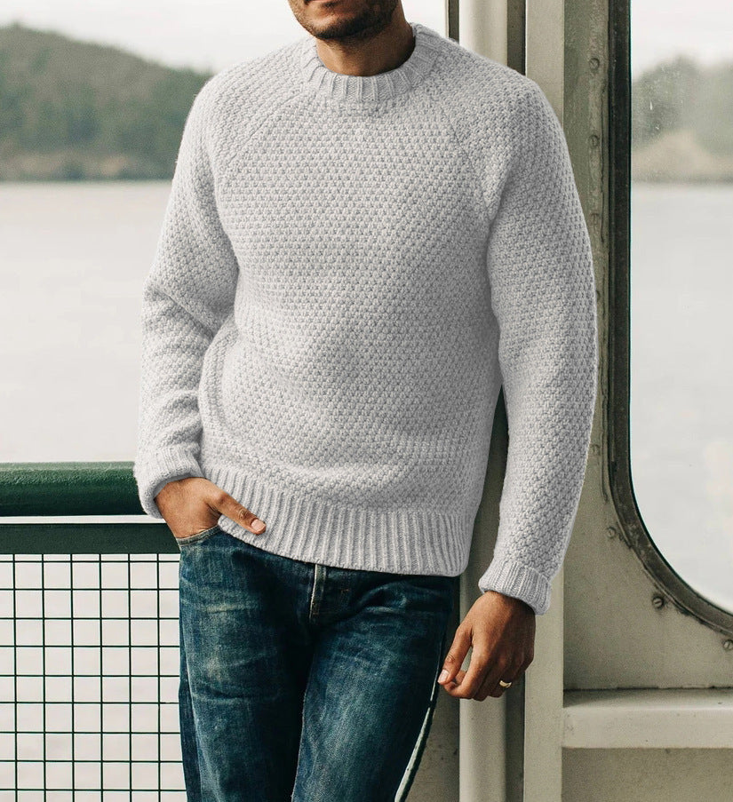 Man wearing light gray knitted men's pullover sweater with round neck and blue jeans indoors by window