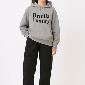 Woman wearing black solid color high waist cargo trousers with multiple pockets, paired with a grey Briella Luxury hoodie and black bucket hat.