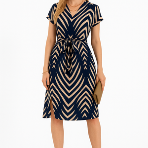 Woman wearing navy and beige striped midi dress with V-neck and tie waist, styled with nude heels and clutch, standing against white background