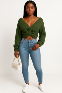 Woman wearing solid color long sleeve knotted green knitwear sweater paired with jeans and white sneakers, holding a white handbag.